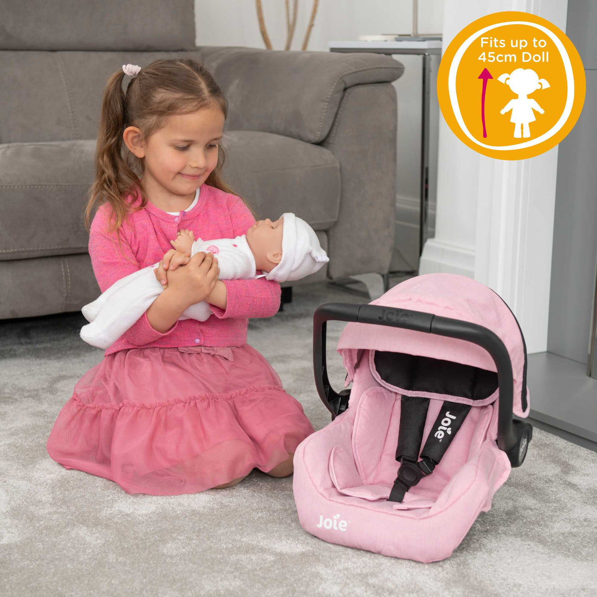 Joie I-Gemm Dolls Car Seat in pink and black, featuring a realistic design with secure harness, padded interior, and carry handle, perfect for children to safely transport their dolls during playtime