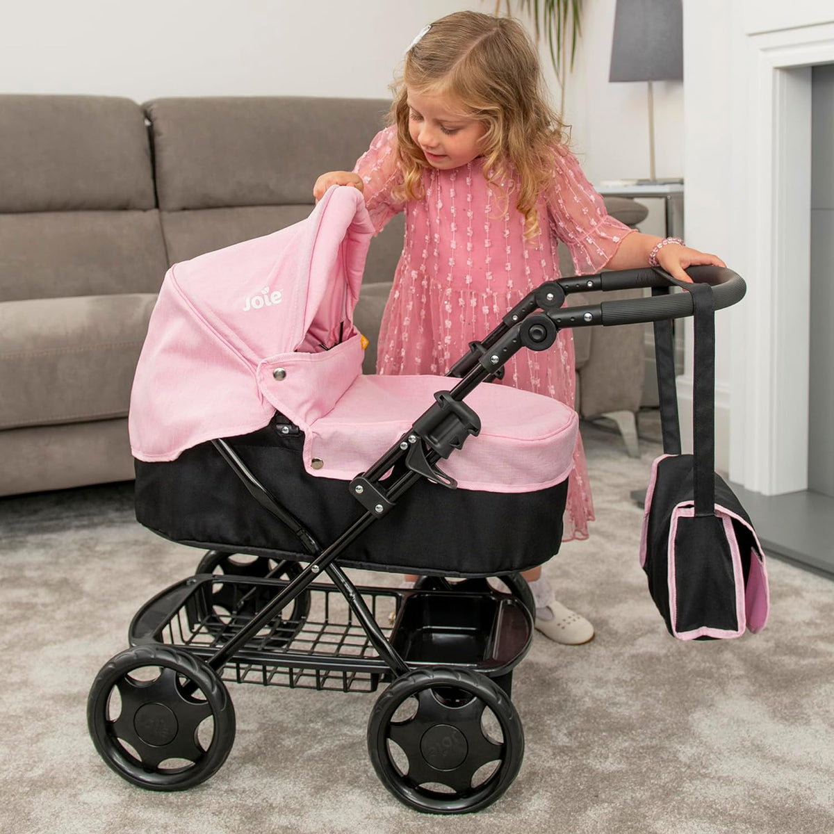 Joie Junior Classic Pram in pink and black, featuring a vintage design, includes a handheld parasol and a matching changing bag, perfect for children to enjoy sophisticated doll play and outings.