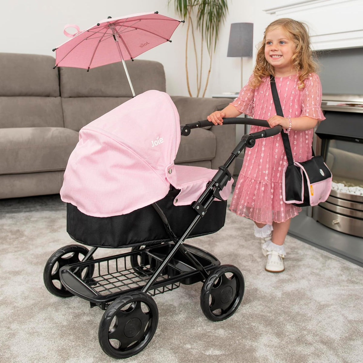 Joie Junior Classic Pram in pink and black, featuring a vintage design, includes a handheld parasol and a matching changing bag, perfect for children to enjoy sophisticated doll play and outings.